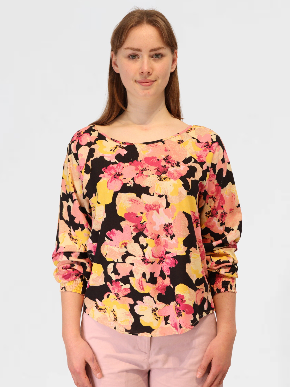 Model wearing long sleeve floral blouse in pink, yellow, and black tones, styled with blush trousers.