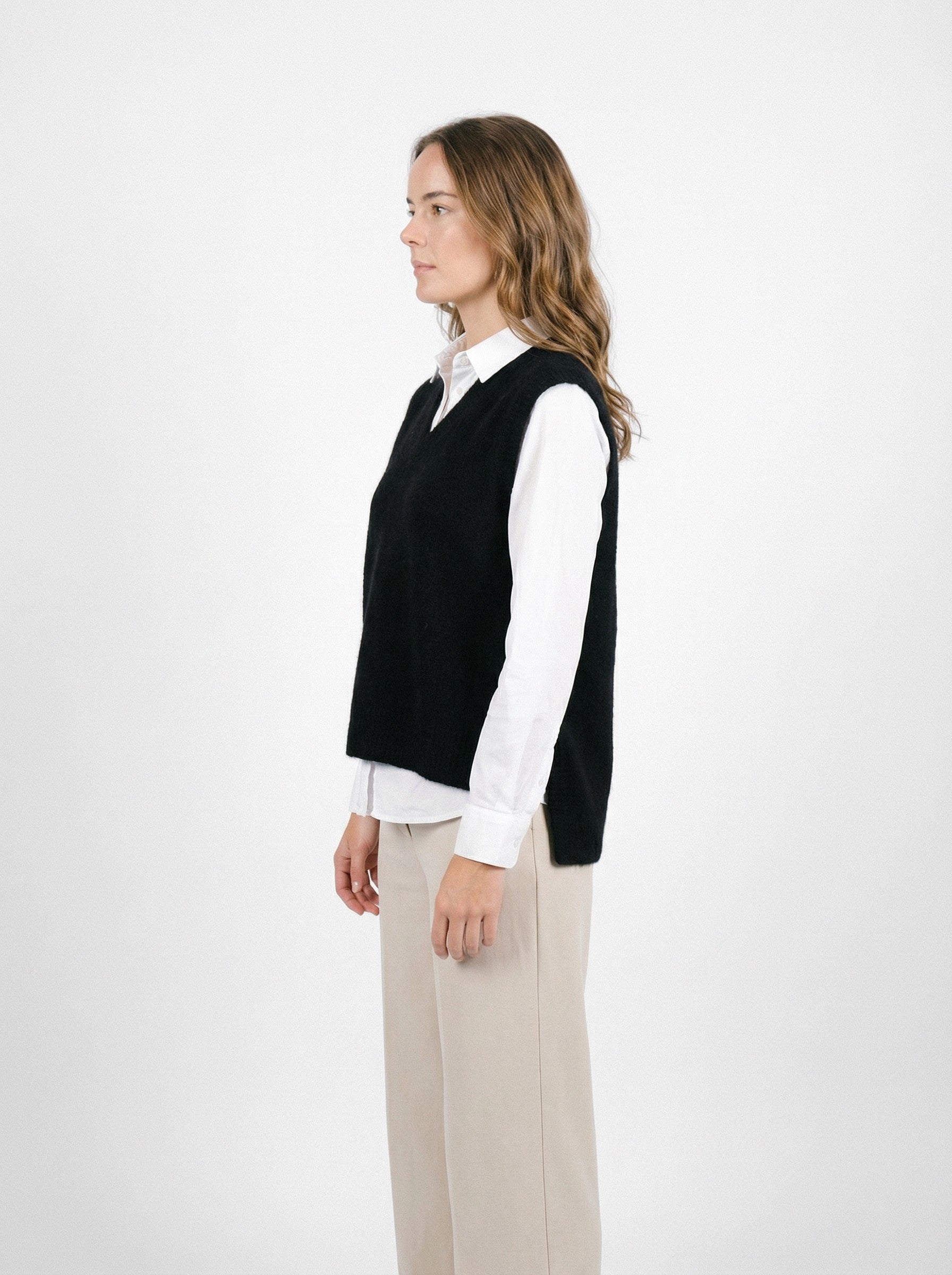 Woman wearingPossum Merino Ride Vest - Black over white shirt and beige trousers, side view