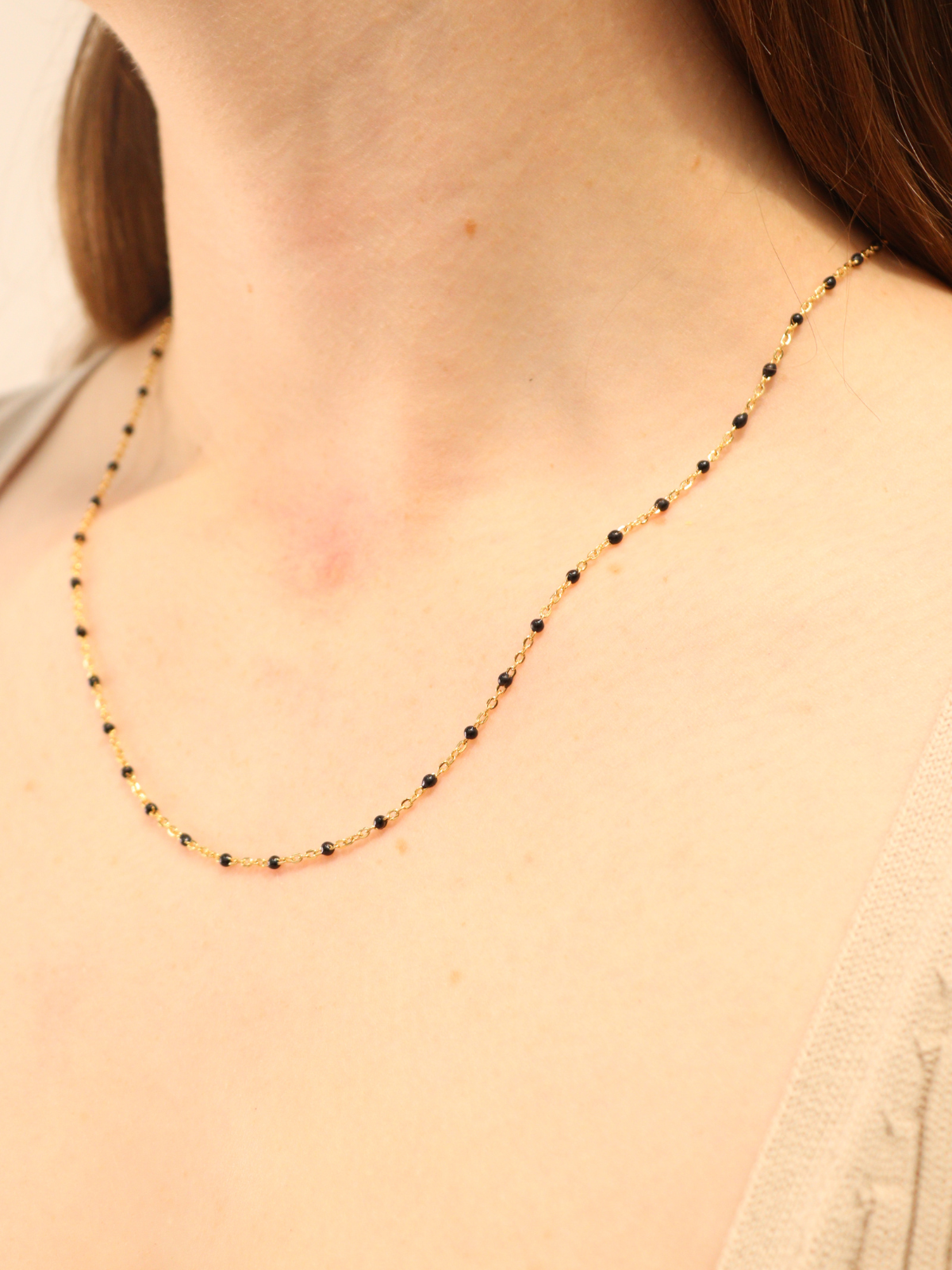 Gold chain necklace with evenly spaced black beads, worn on neck.