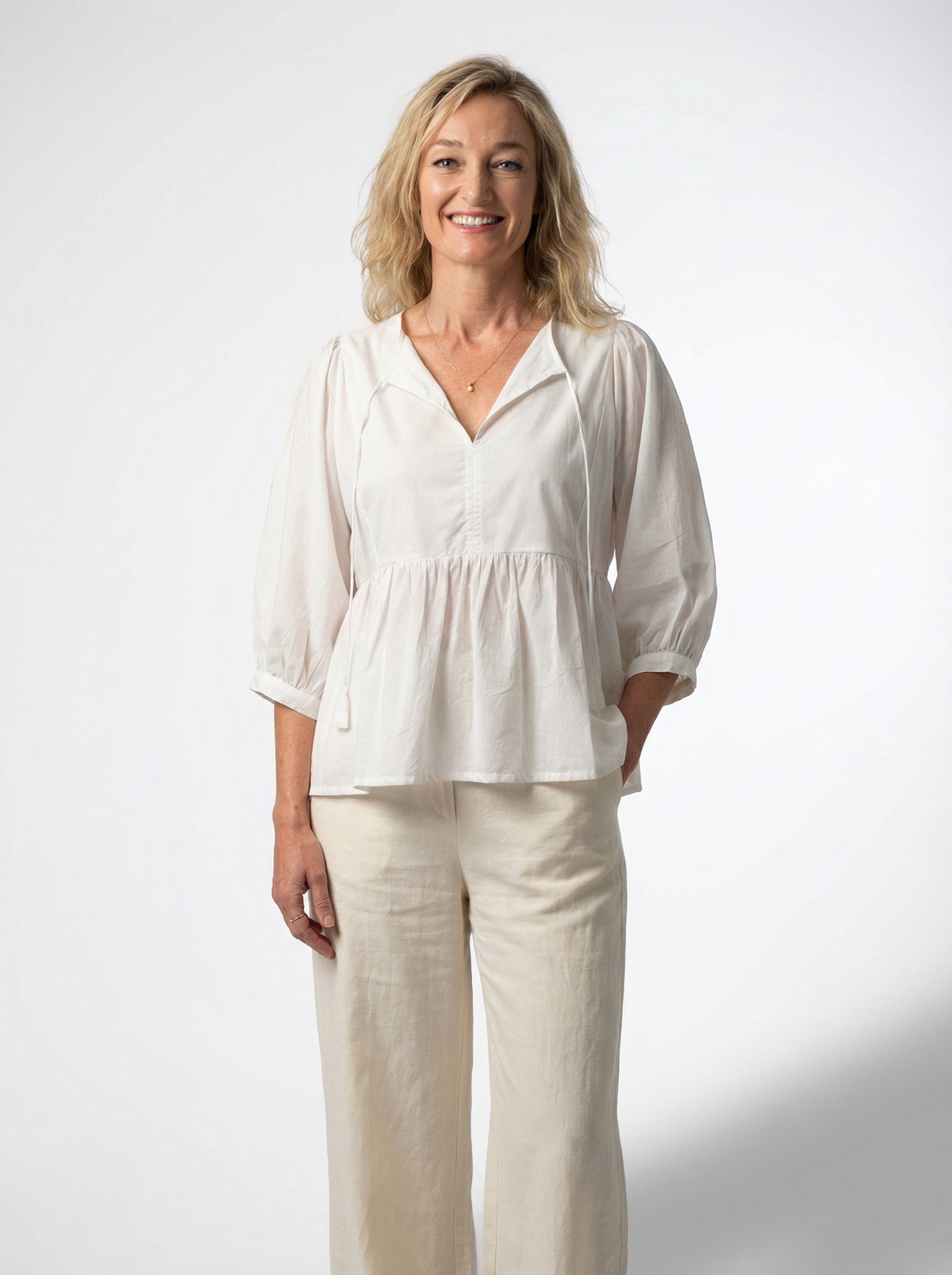 Woman wearing a white blouse from Reca called (Dream Fields Cotton Top) and beige pants against a white background