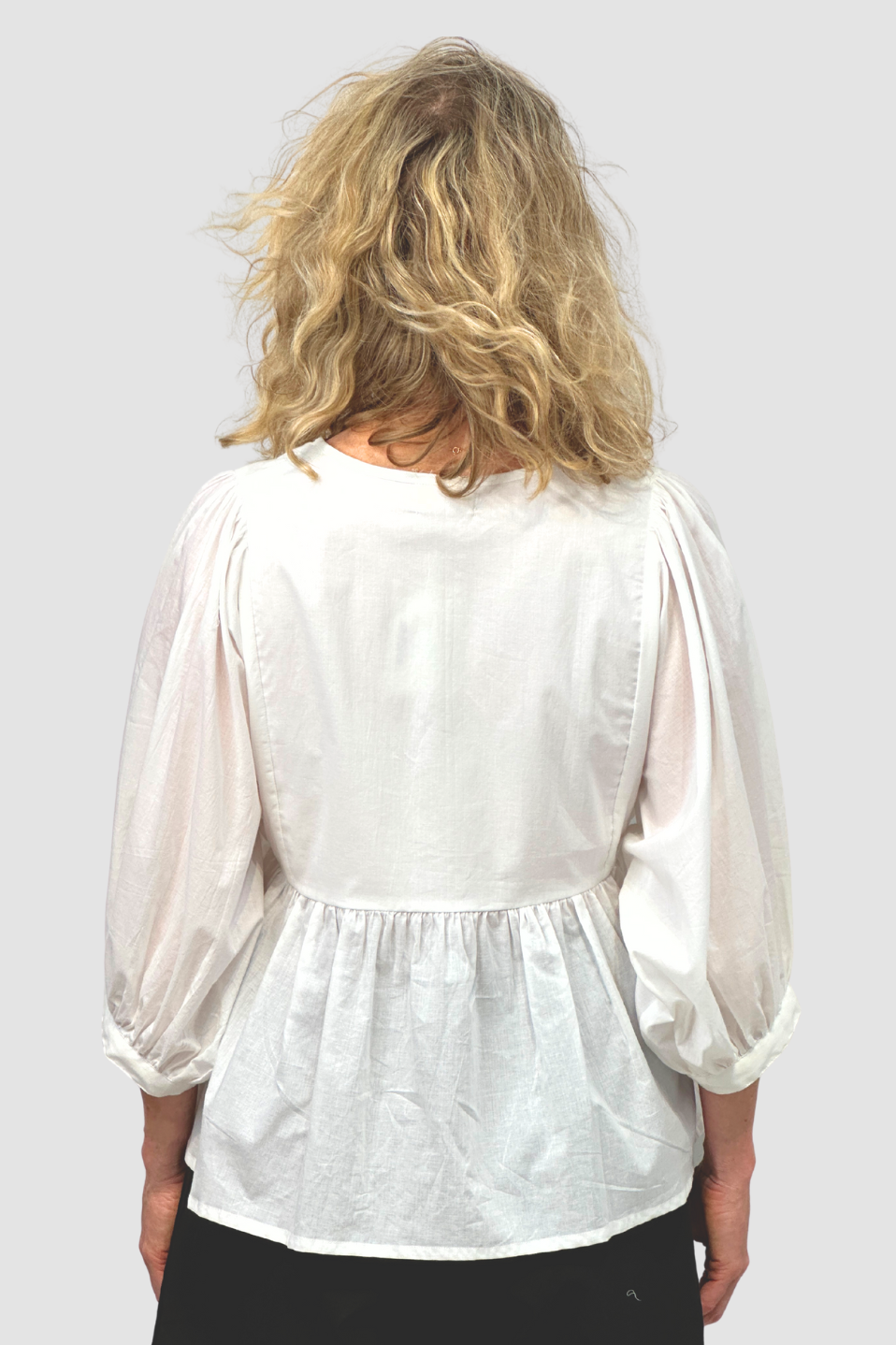 Back view of woman with wavy blonde hair wearing a white puff sleeve blouse