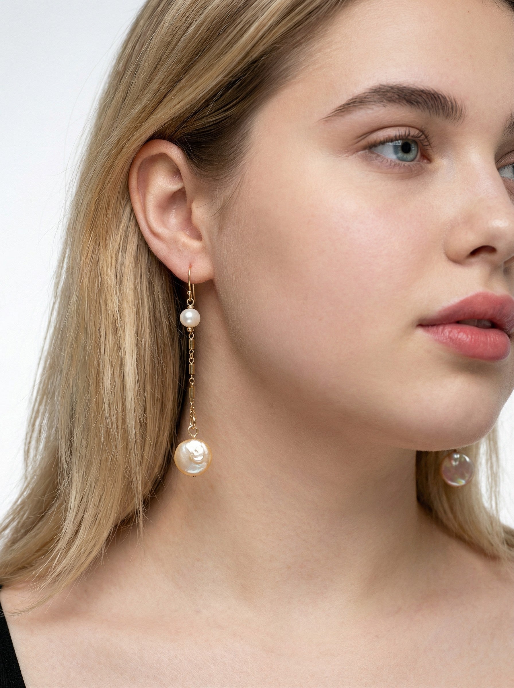 Close-up of a woman wearing  Gold Duo Pearl Earrings with a plain background