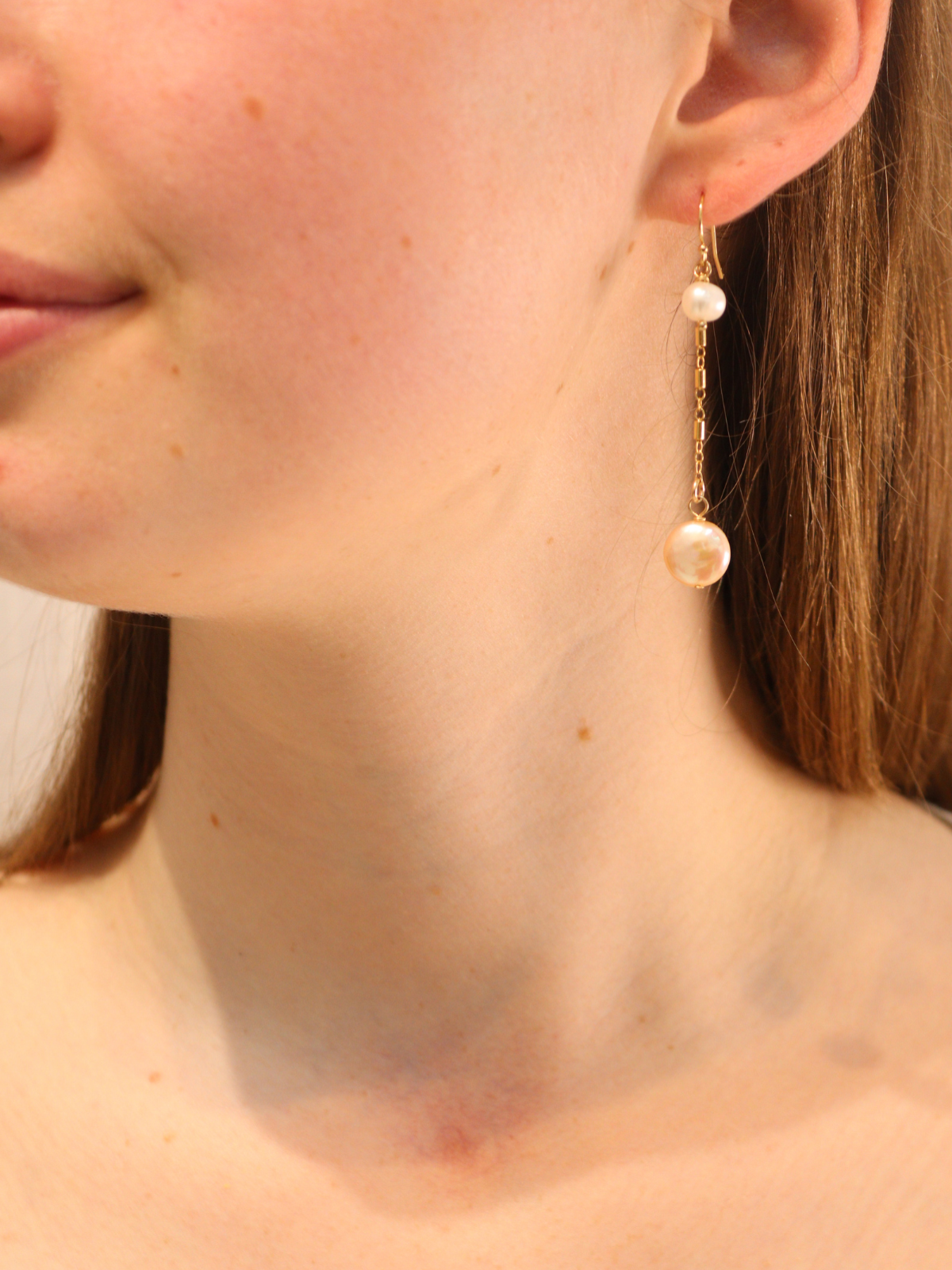 Gold chain drop earring with two pearls, worn on ear.
