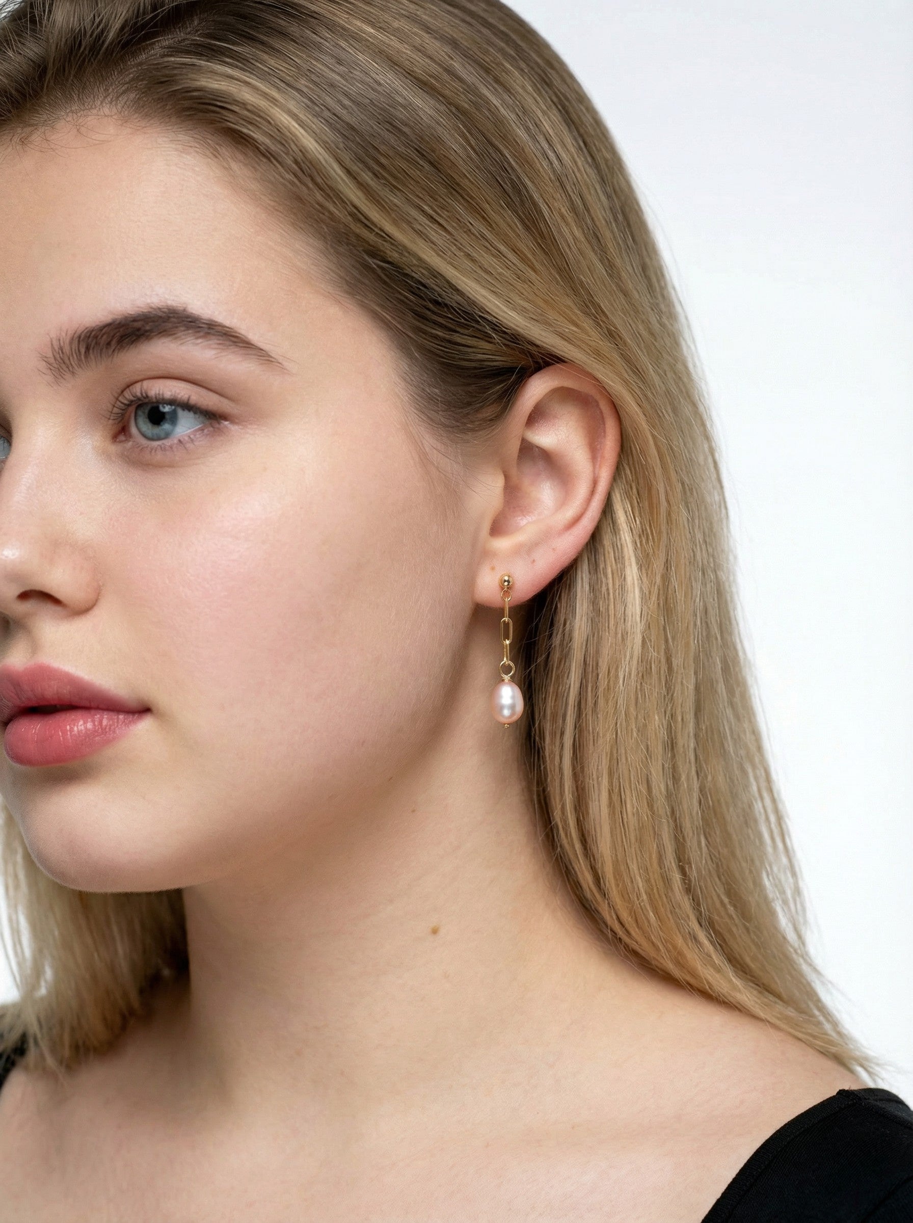Close-up of a woman wearing Gold Paperclip Pearl Earrings
 with a plain background