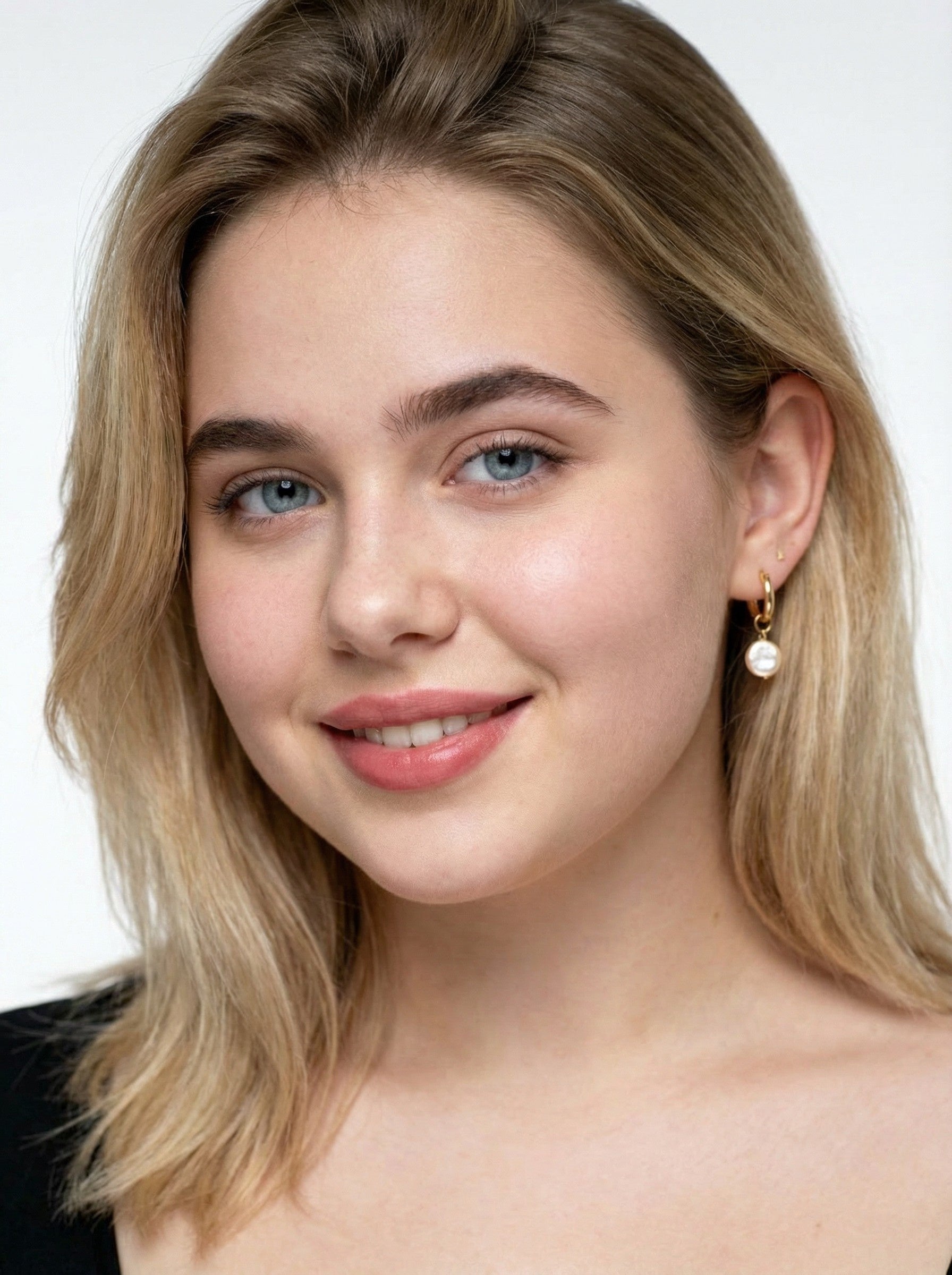 Close-up of a person with blonde hair and hoop with pearl earring on a white background