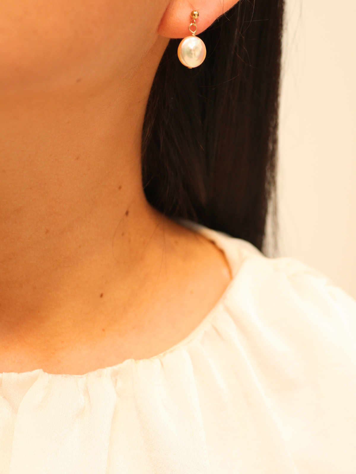 Gold drop earring with single round pearl, worn on ear.