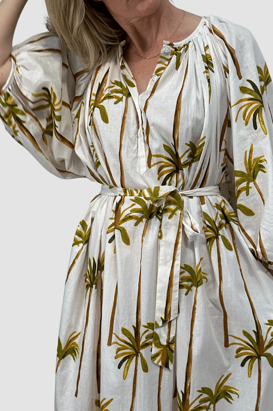 White dress with palm tree pattern worn by a person with belt, on a plain background