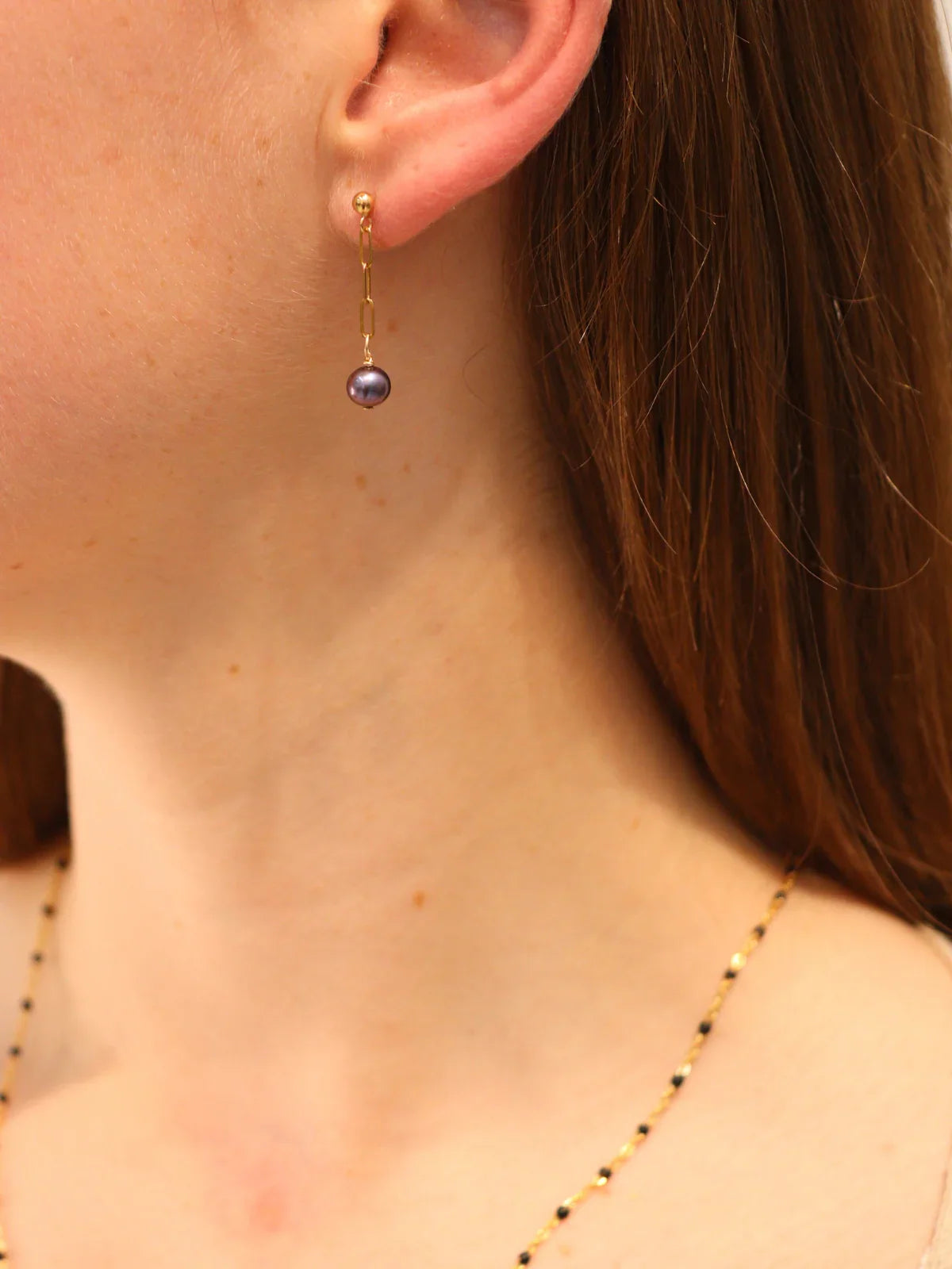 Gold link drop earring with single black pearl, worn on ear.
