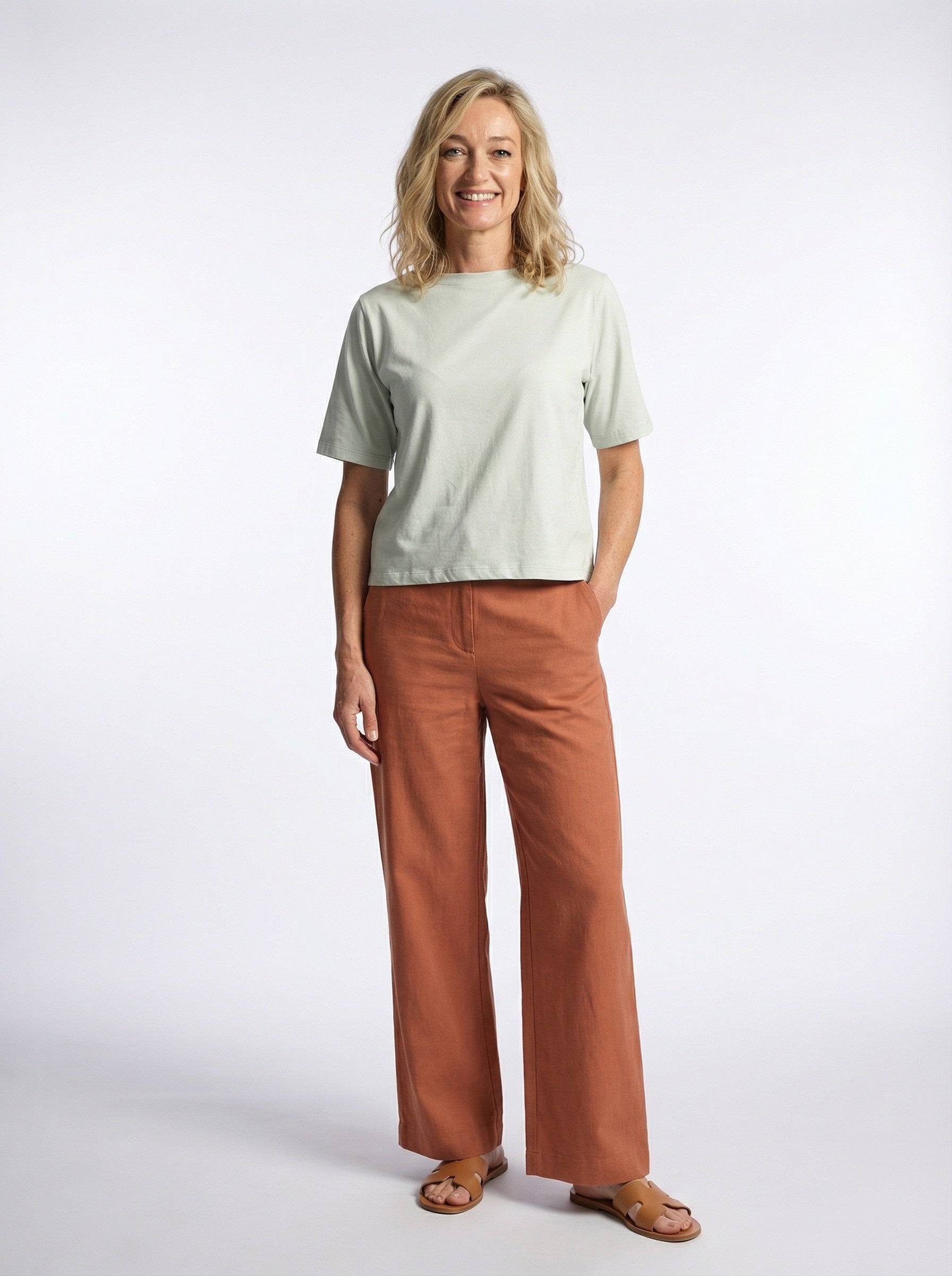 Woman wearing a Organic Flex Crew Tee - Pale Turquoise and brown pants on a white background