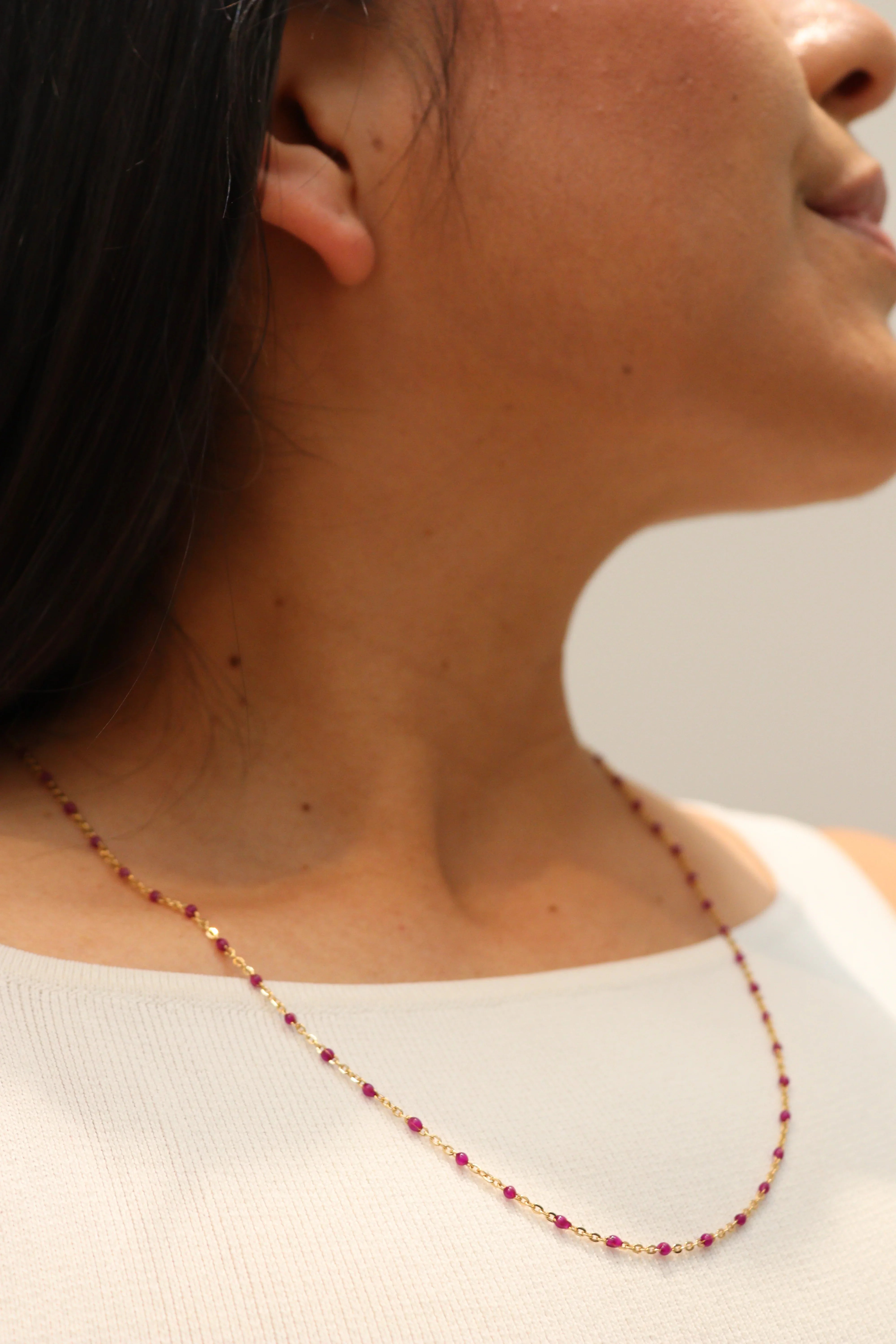 Close-up of a person wearing a gold red beaded necklace with a neutral background