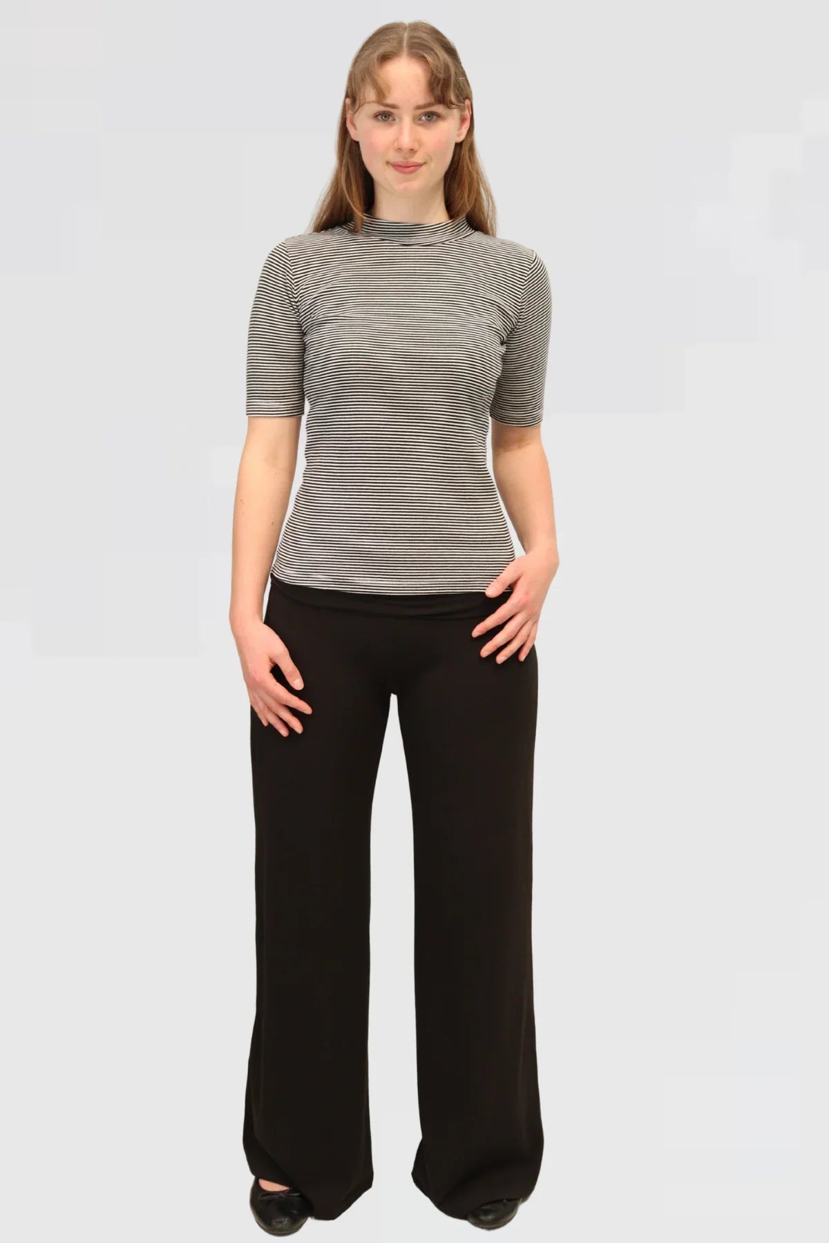 Model wearing Reca’s Leisure Lux Pants in black, wide-leg style with a relaxed high-waisted fit, paired with a striped top.