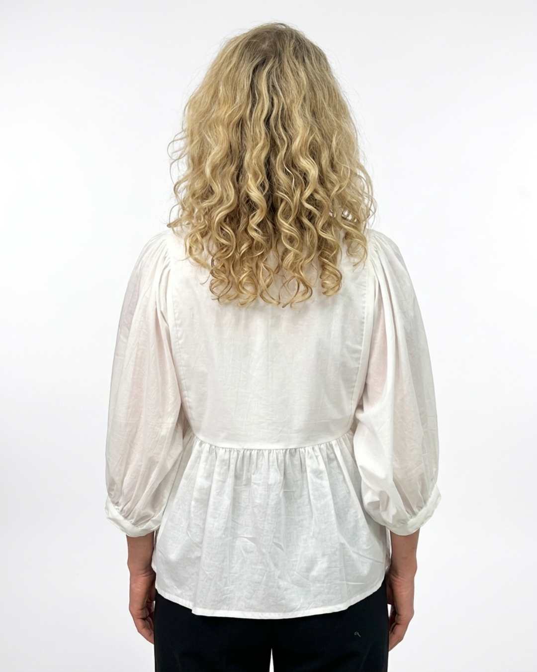 Back view of a woman wearing a white cotton blouse with three-quarter blouson sleeves and a gathered peplum waist