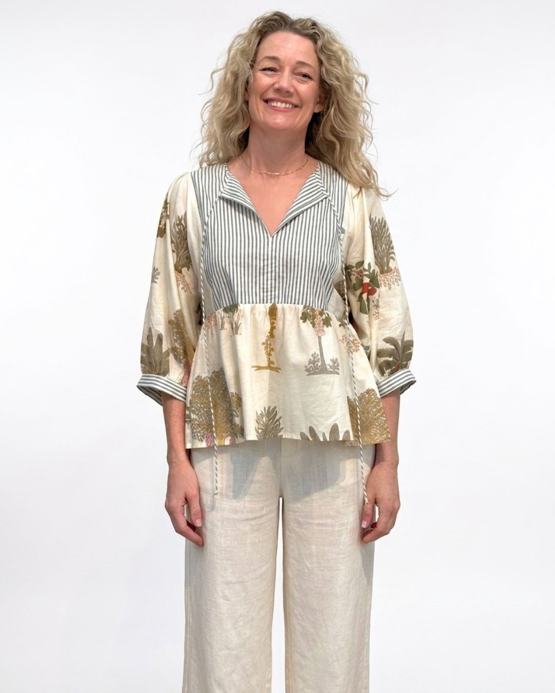 Full-length front view of a woman wearing the Reca Botanica Luxe Cotton Blouse with cream wide-leg linen pants