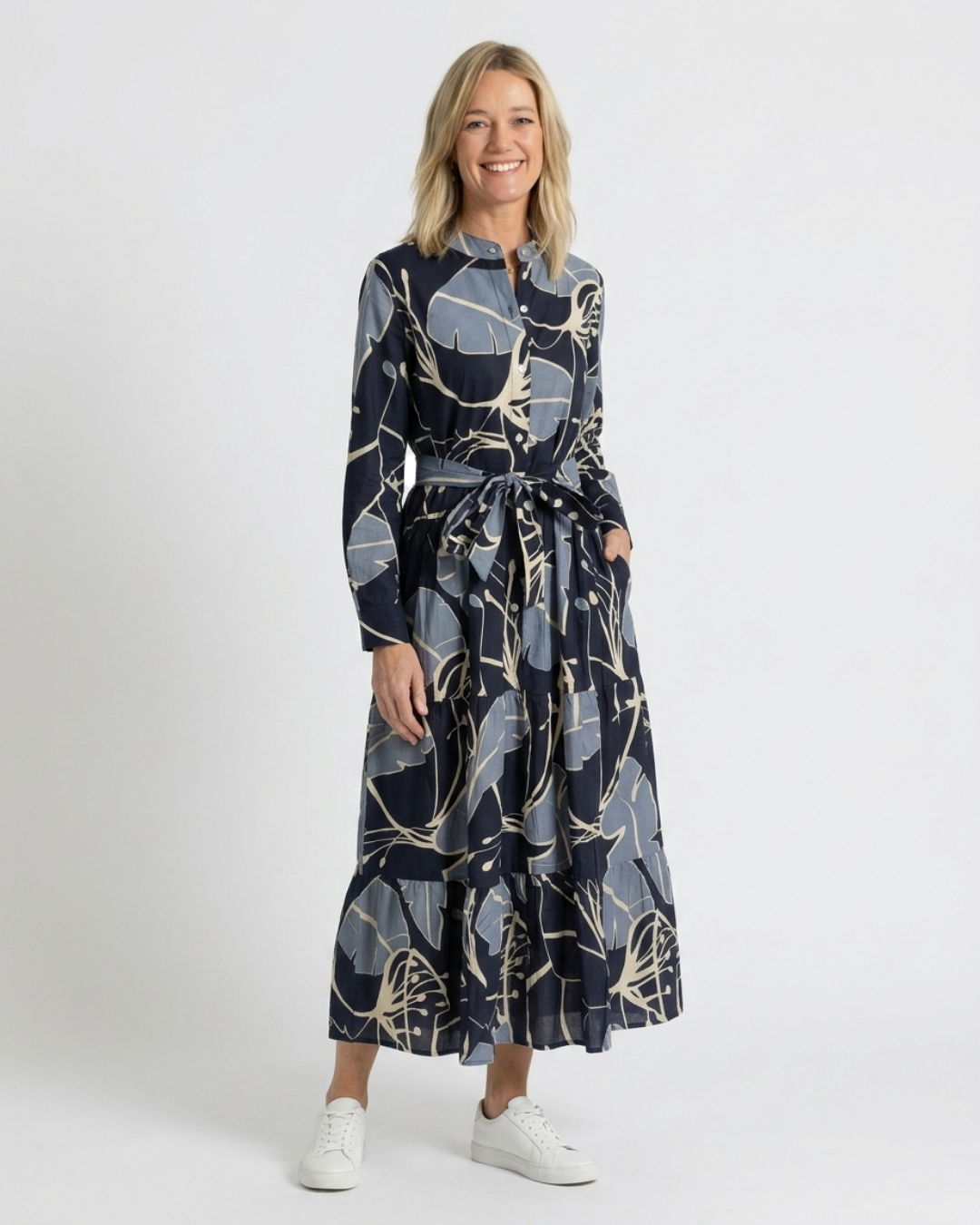 Woman wearing the Reca Indigo Bloom navy botanical print cotton midi dress, belted at the waist, full length front view with white sneakers