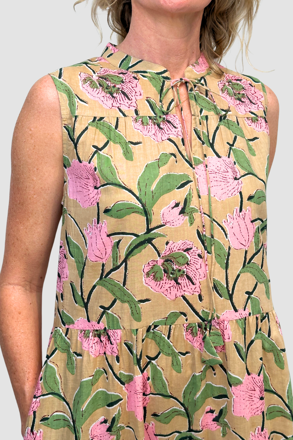 Woman wearing a sleeveless dress with pink floral pattern on a plain background