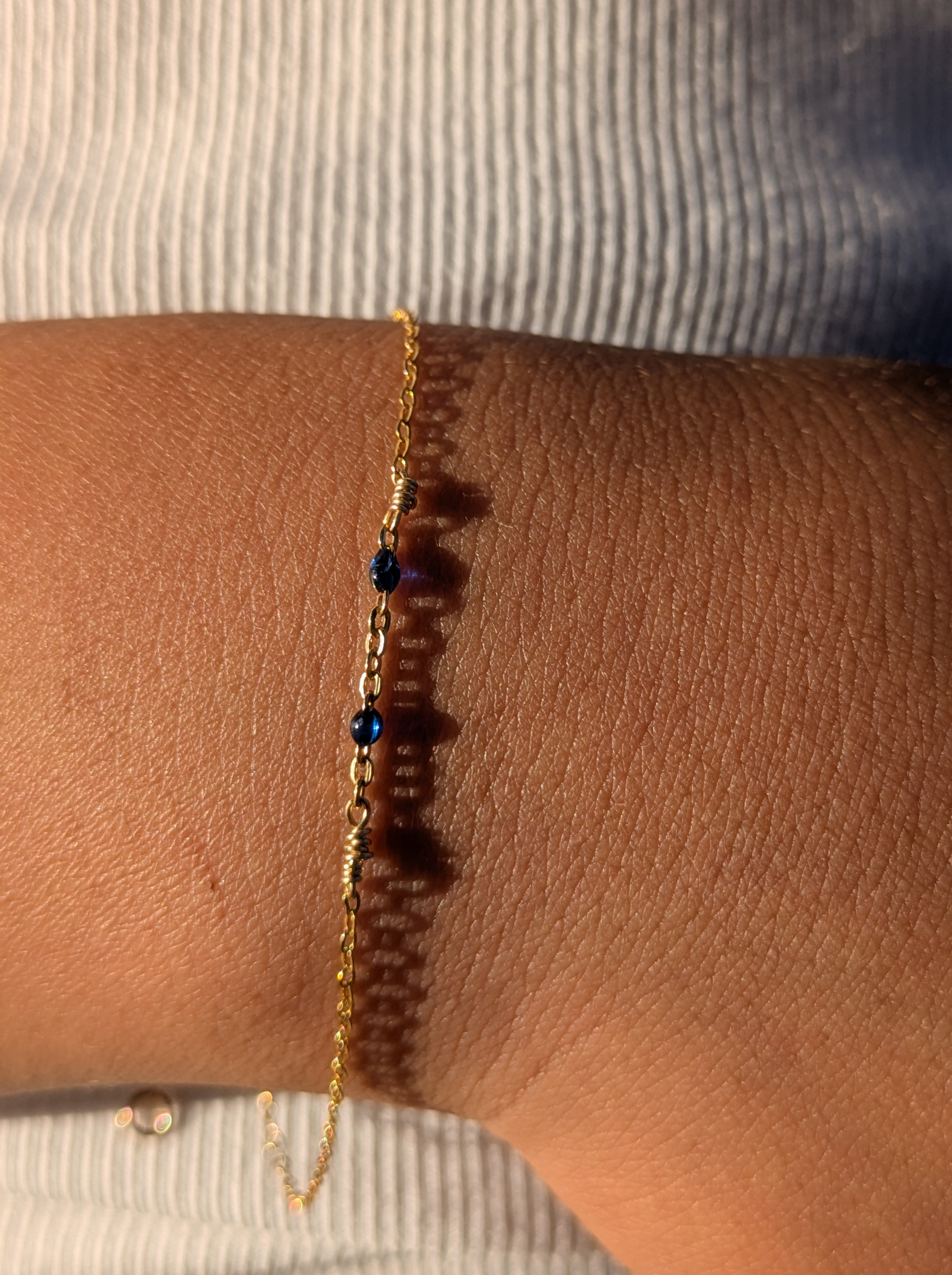 Delicate gold chain bracelet with blue beads on wrist, ethical Reca jewellery