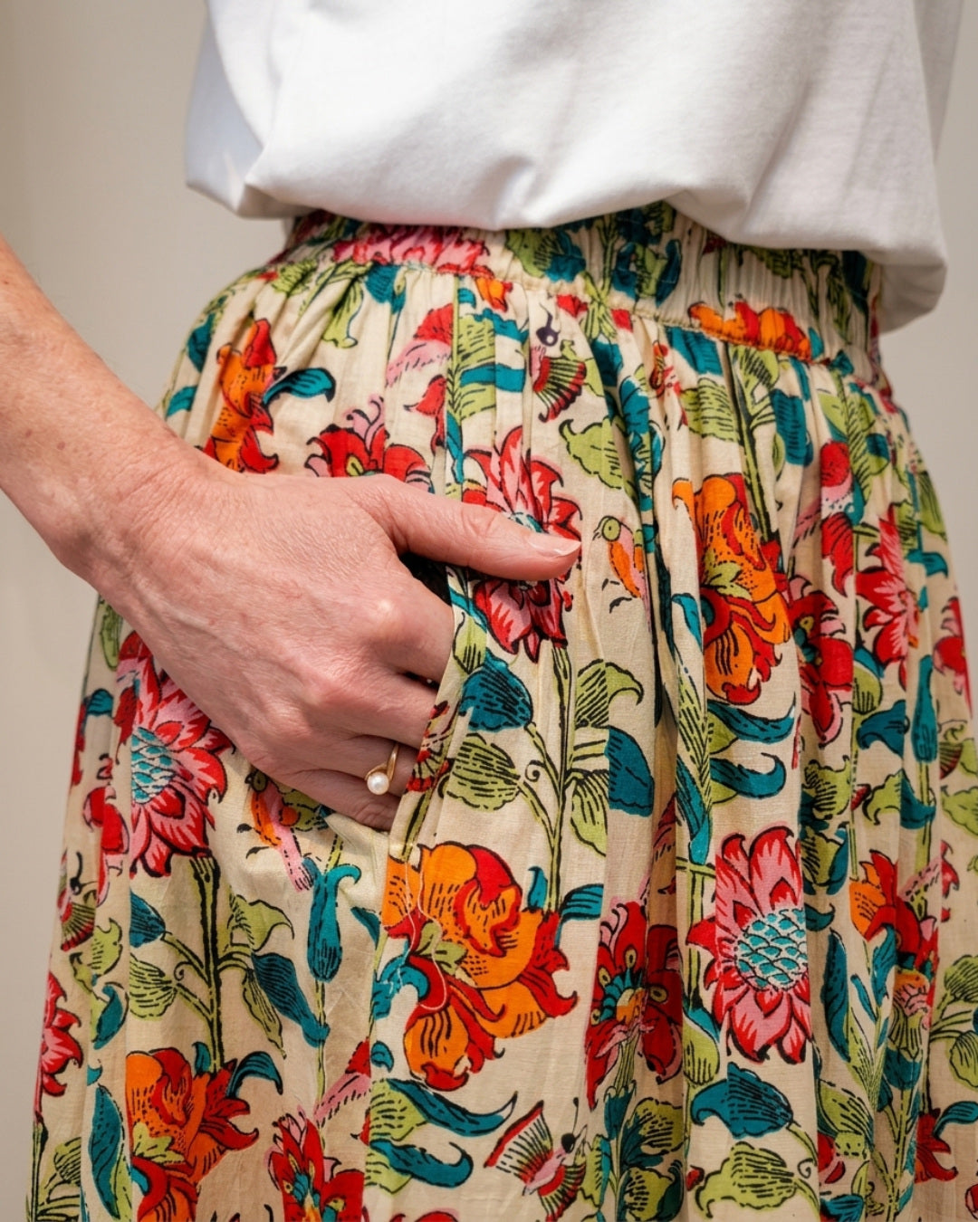 Close-up of the Bloomfield Garden Skirt with a hand in the deep side-seam pocket, showing the gathered elasticated waistband and cotton floral print