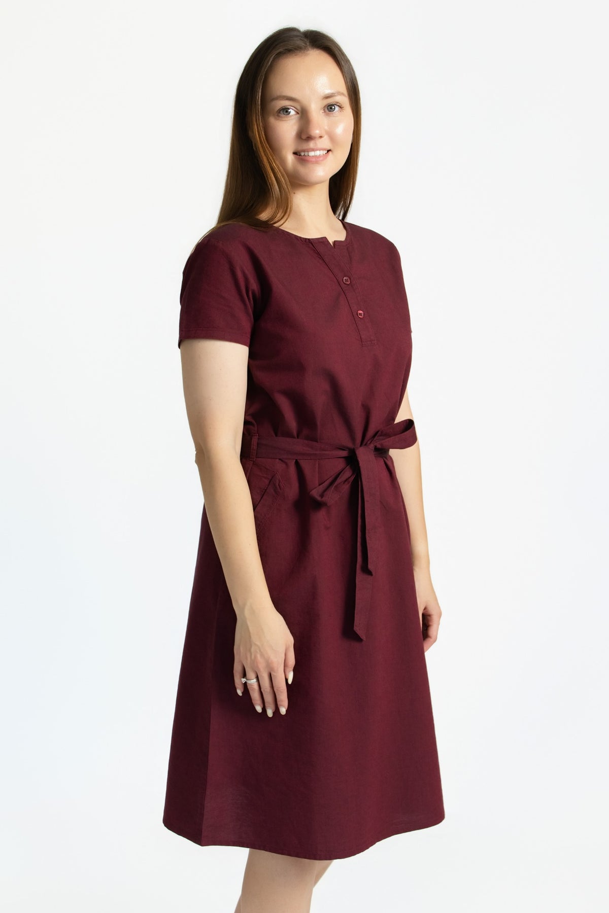 Angled view of a burgundy linen cotton dress with short sleeves, removable belt and side pockets