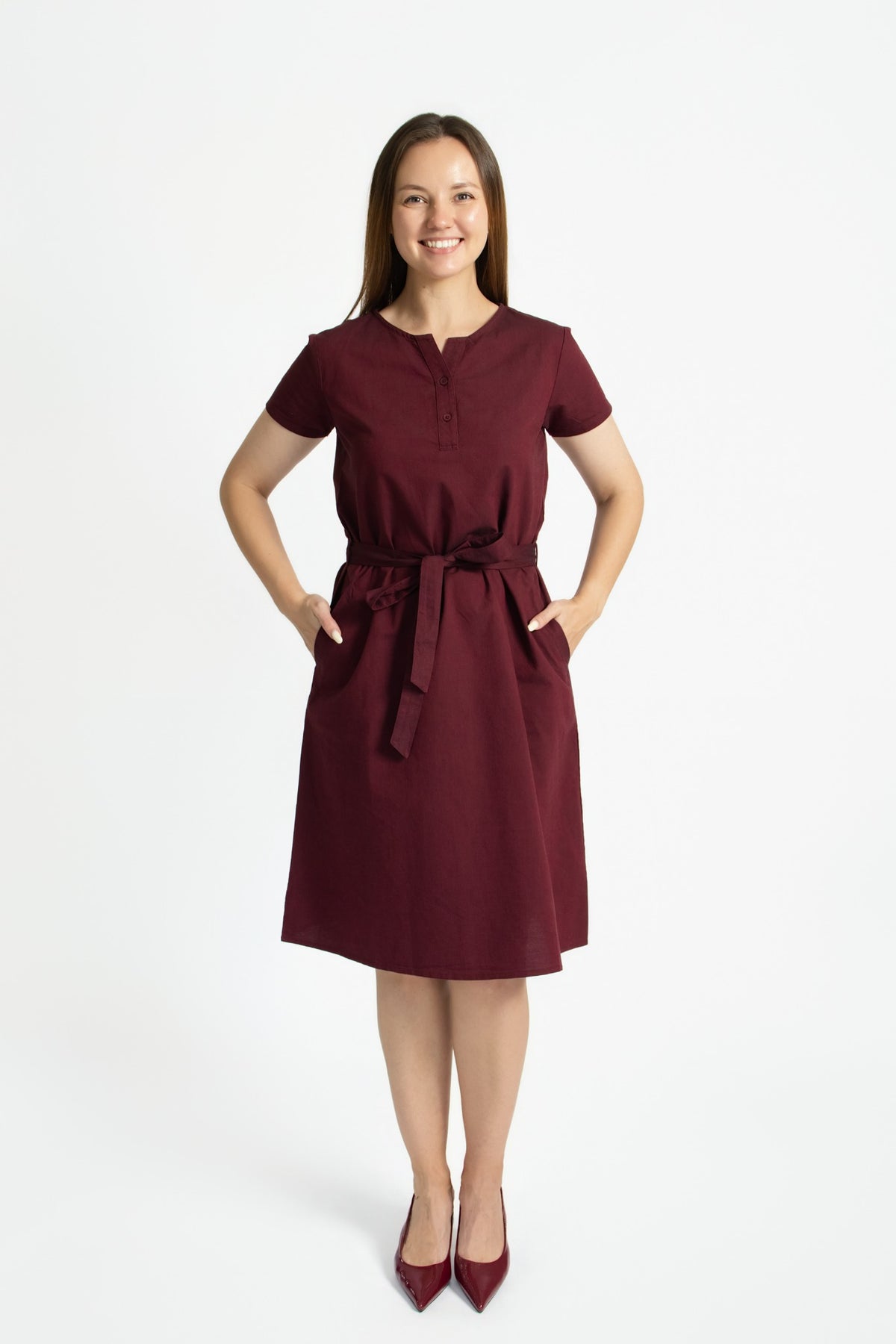 Woman wearing a burgundy linen cotton dress with a removable waist tie and side pockets, front view
