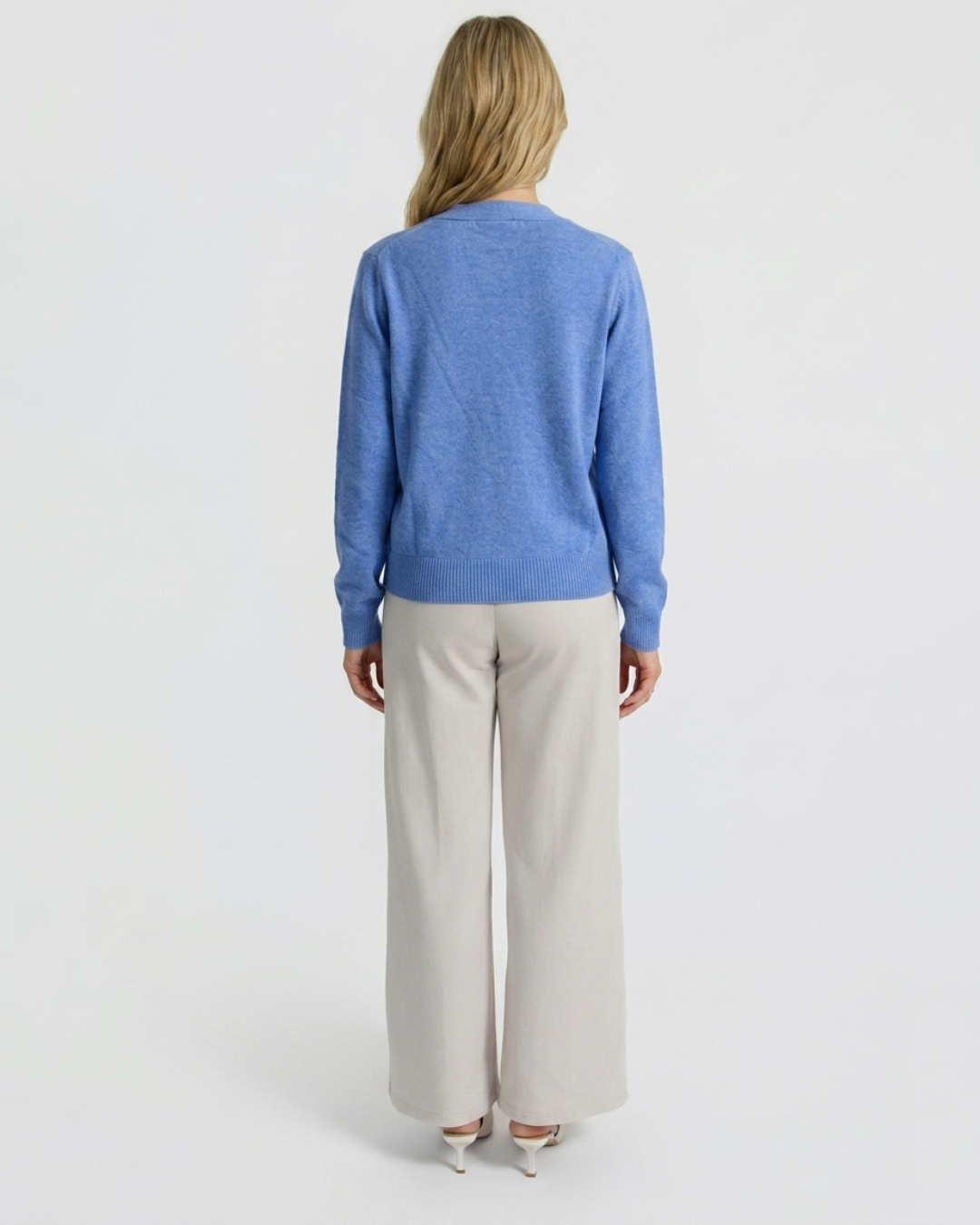 Back view of the denim blue Cashmere-Merino cardigan showing the raglan shoulder line, worn with cream wide-leg trousers