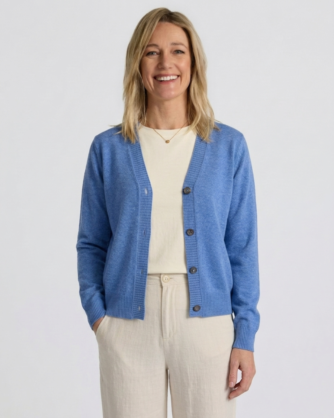 Woman wearing the denim blue Cashmere-Merino cardigan over a cream tee with cream trousers, front view