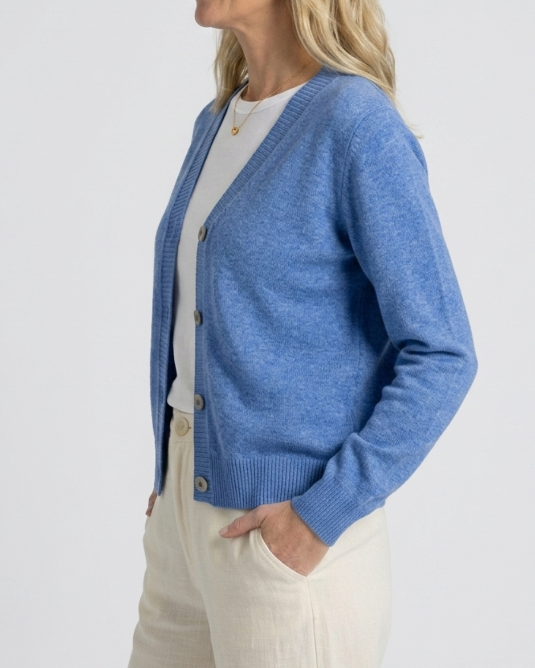 Side view of the denim blue Cashmere-Merino cardigan worn open over a white tee with cream trousers