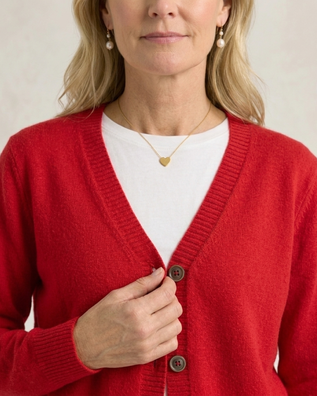 Cropped front view of a woman fastening the buttons on the red Cashmere-Merino cardigan worn over a white tee