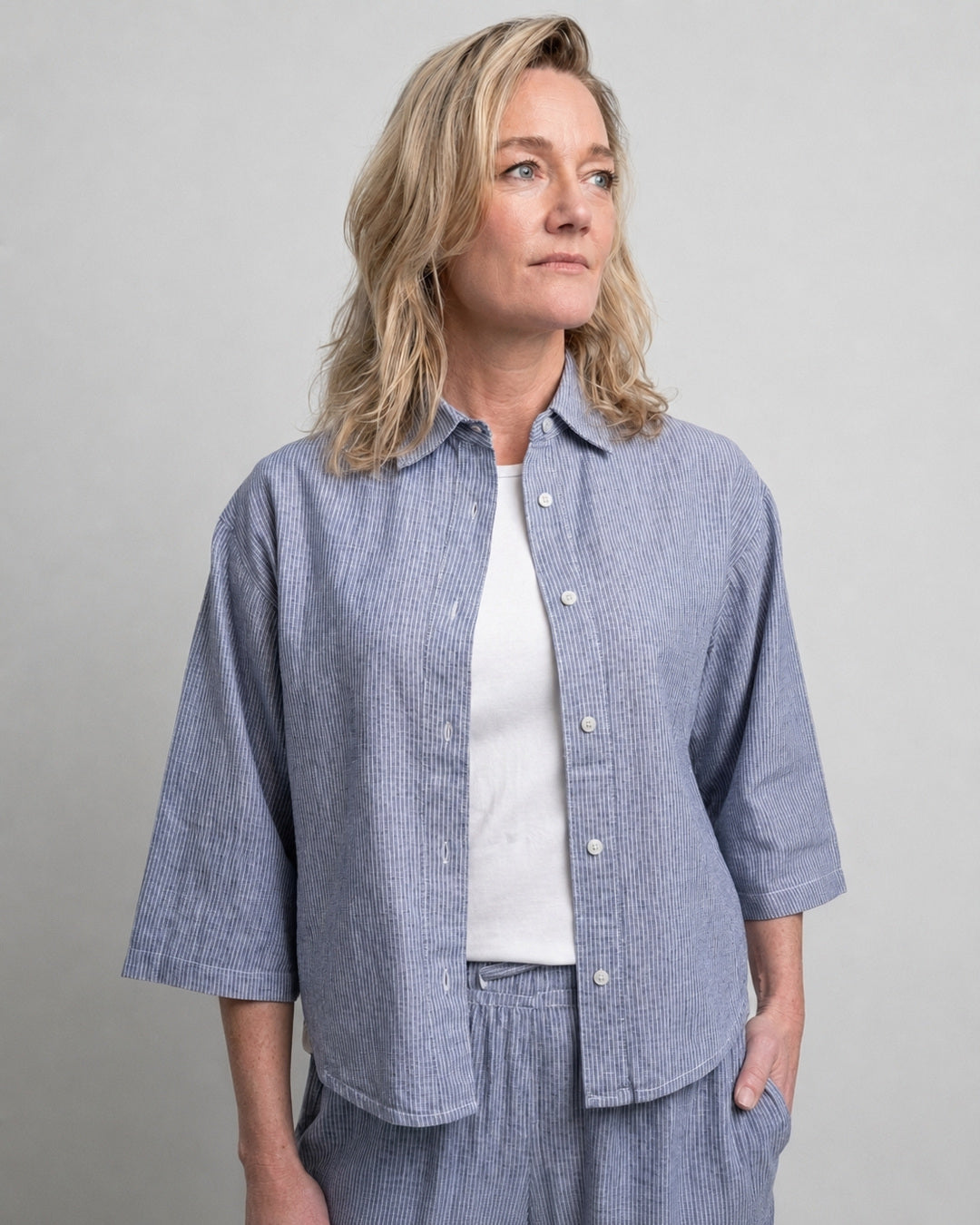 Woman wearing the Reca Cove Linen Crop Shirt in blue and white stripe, worn open over a white tee, front view