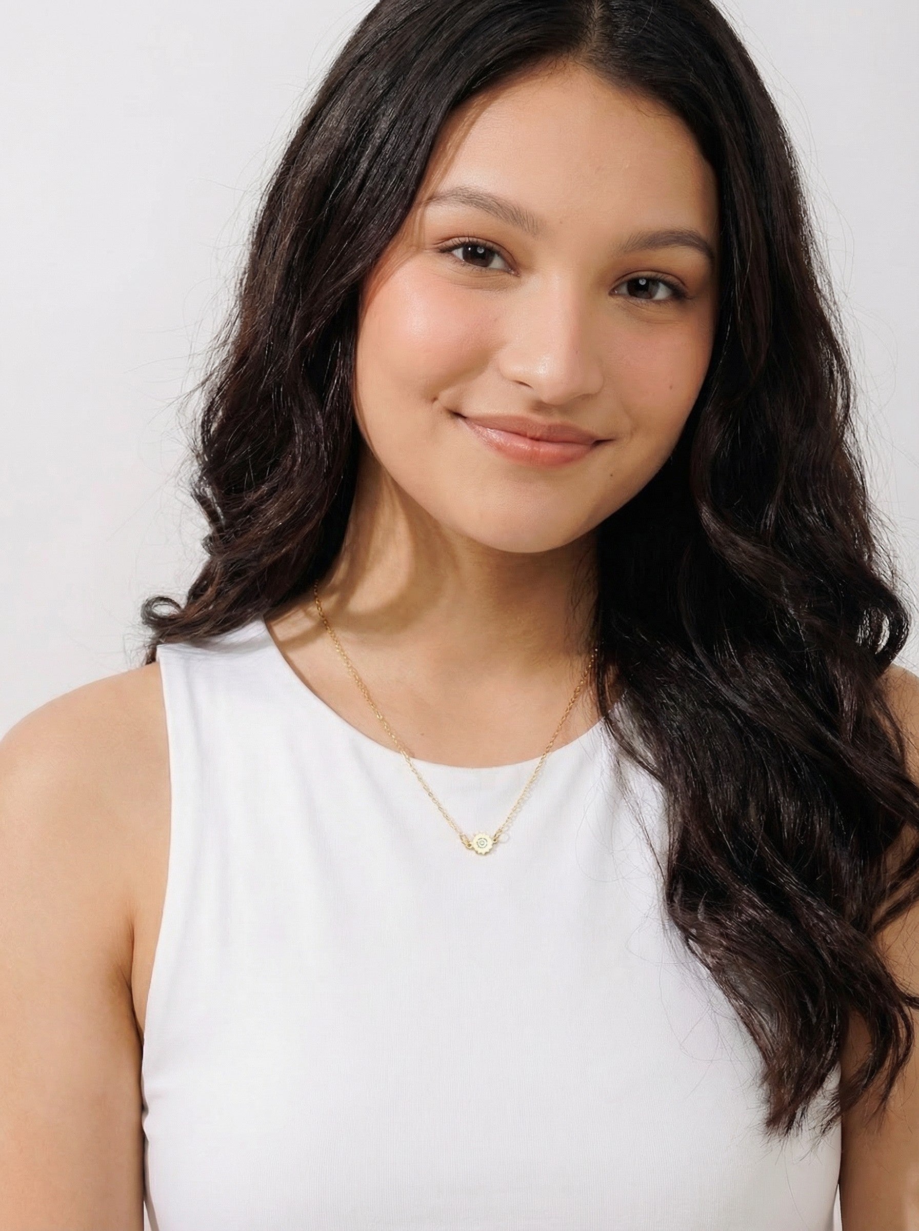 Woman wearing ethical Reca gold necklace with white sleeveless top, simple background