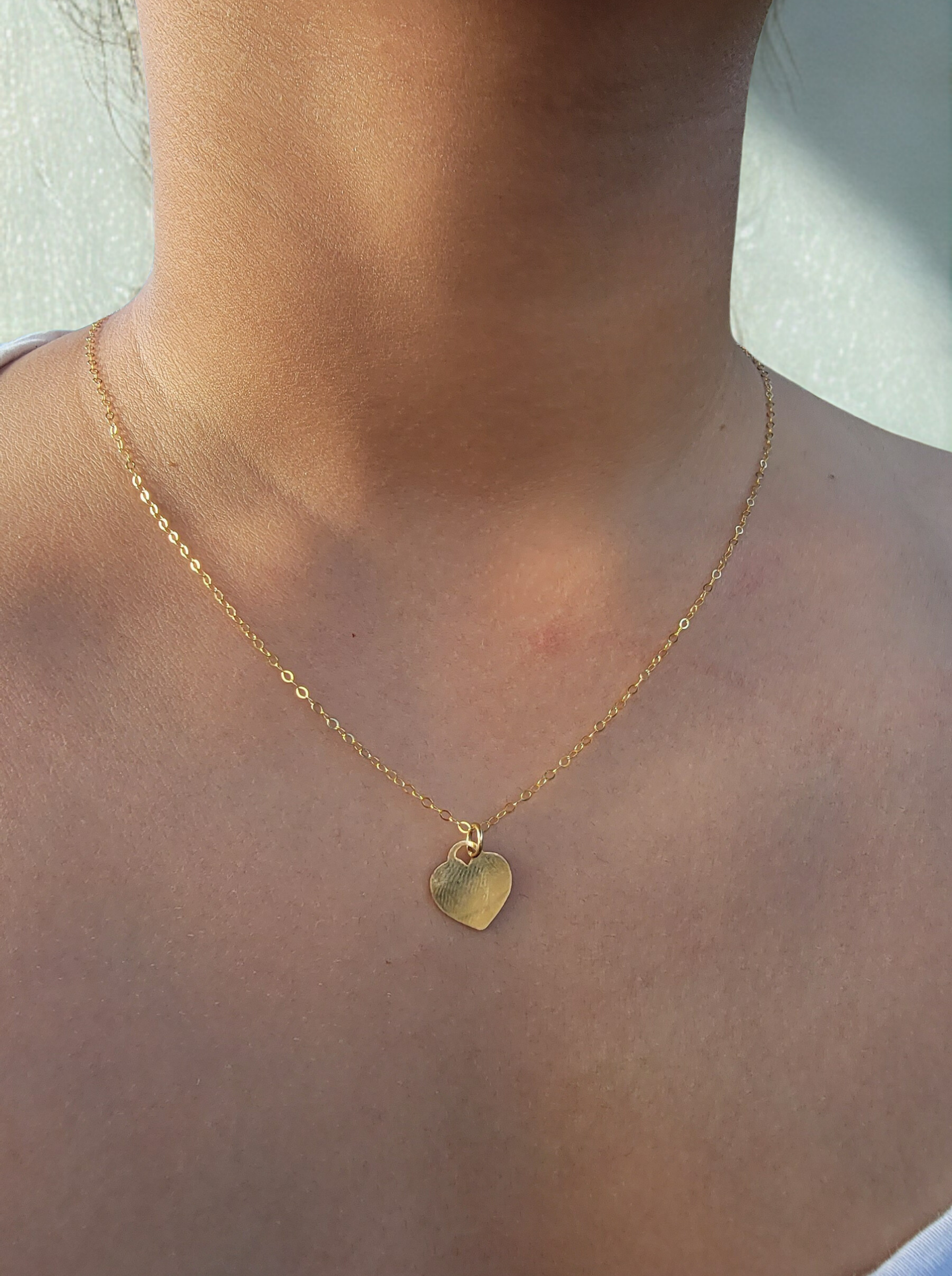 Gold necklace with a heart pendant on a person's neck against a neutral background