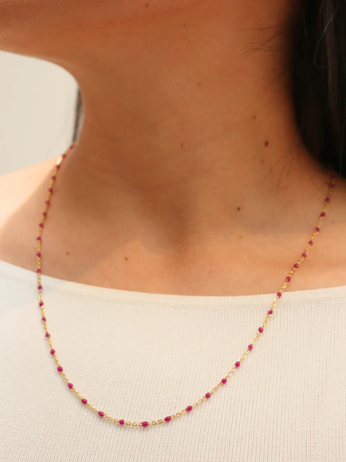 Gold Necklace with red beads worn by a person on a plain background