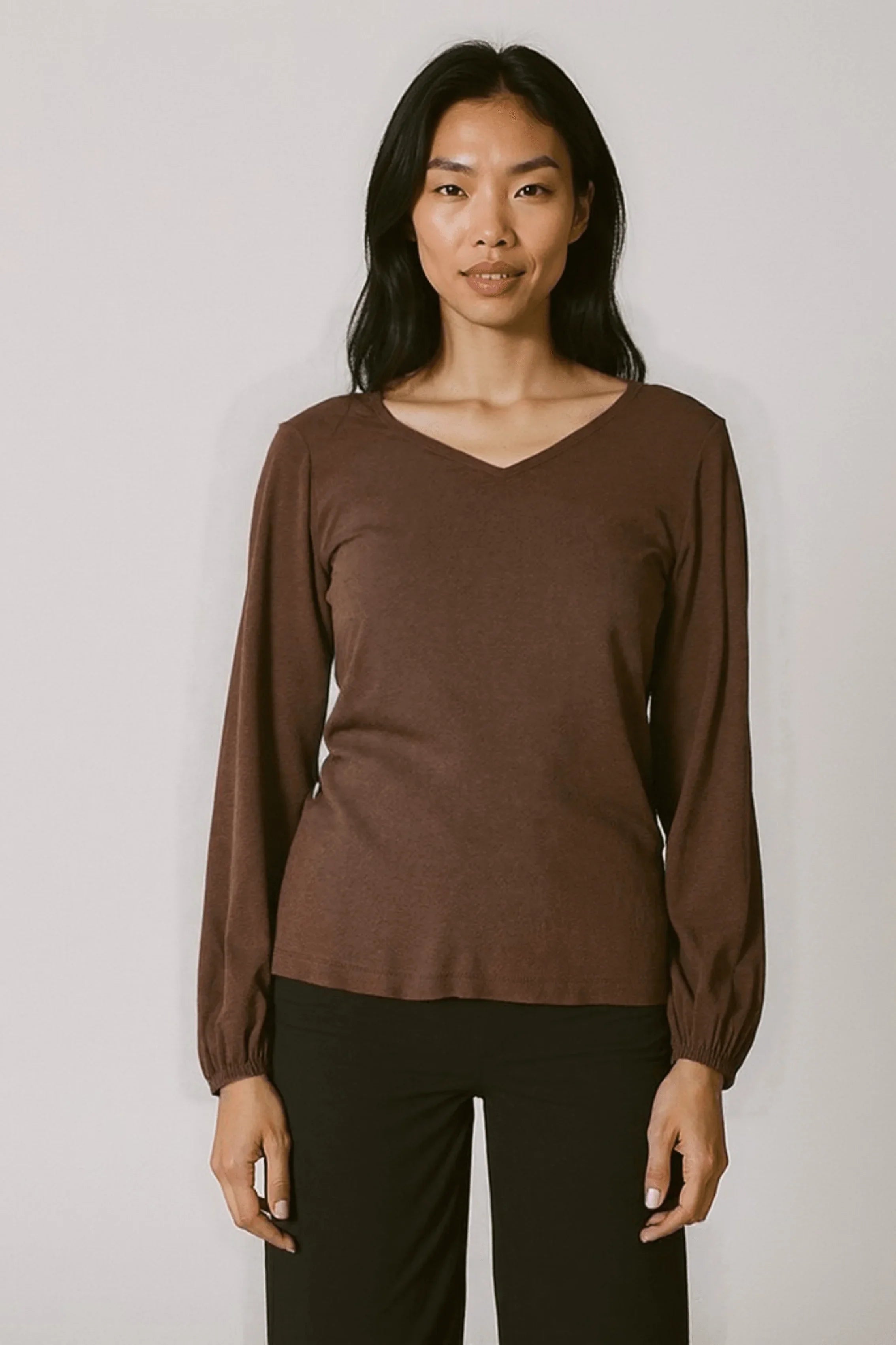 Front view of Reca Bishop Blouse in Redwood, featuring V-neckline and bishop sleeves with gathered cuffs, paired with black trousers.