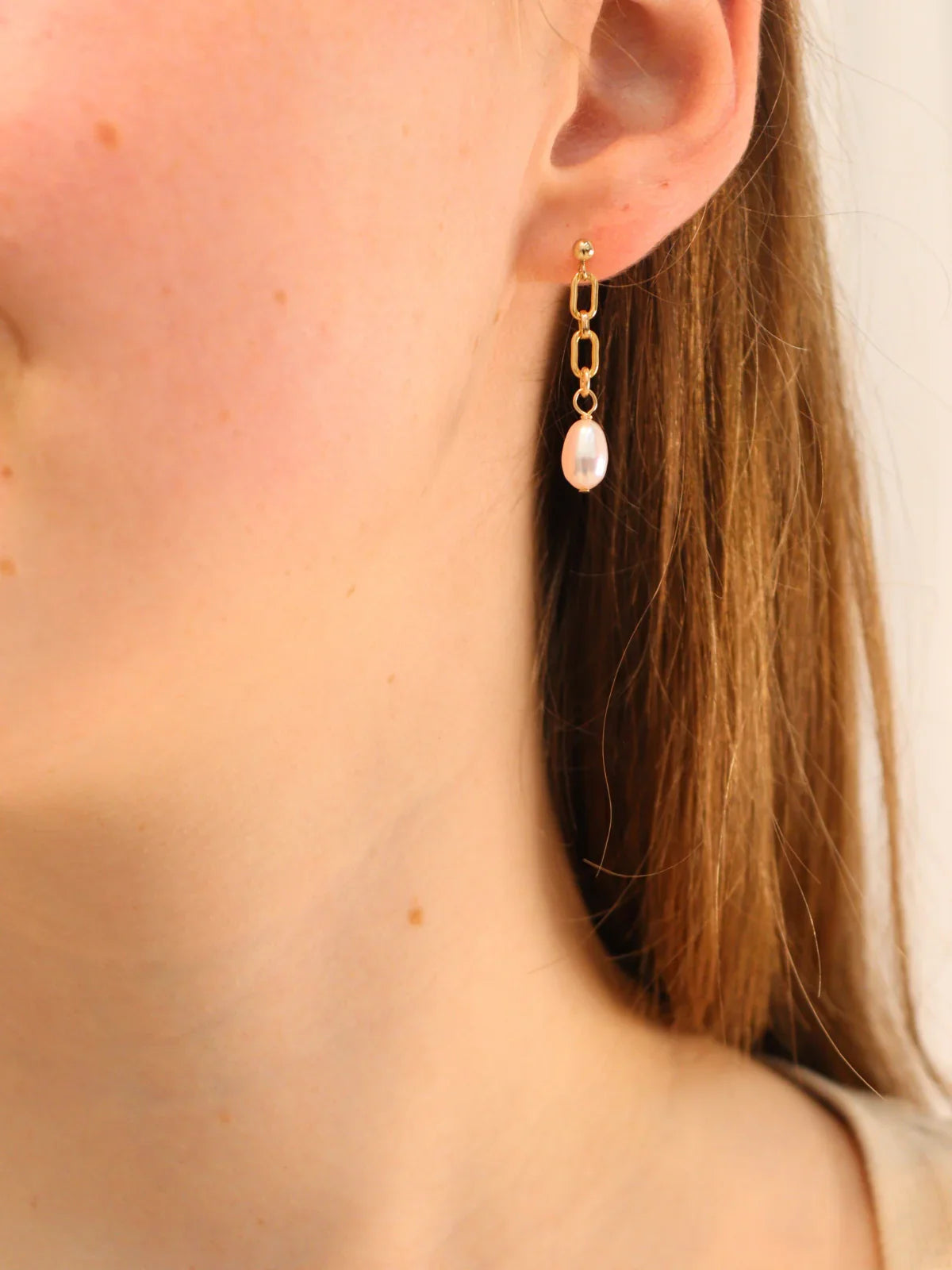 Elegant gold chain link earring featuring a dangling white pearl, shown on ear