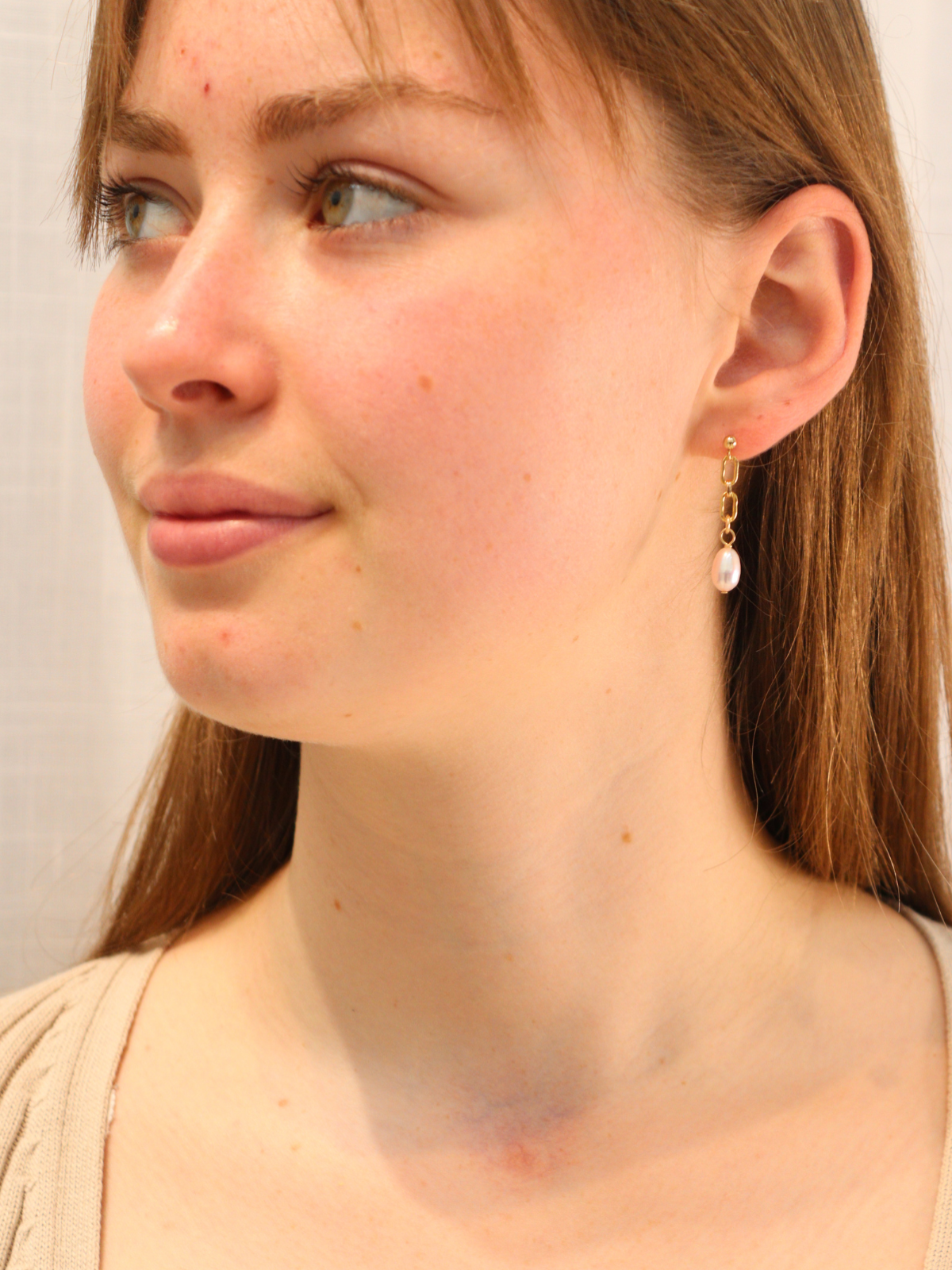 Woman wearing gold chain link drop earrings with white pearl pendants